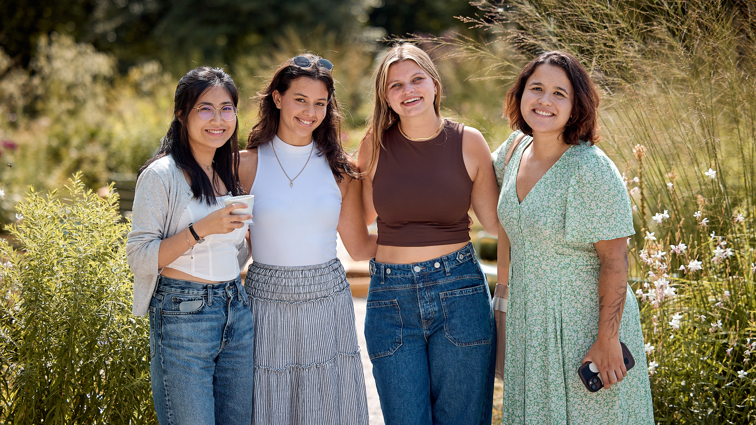 An image of four girls standing outside in a garden and smiling at the camera.