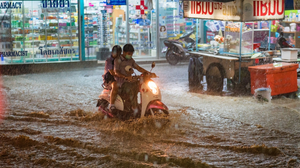 Two people on a motorcycle in a heavily flooded city setting