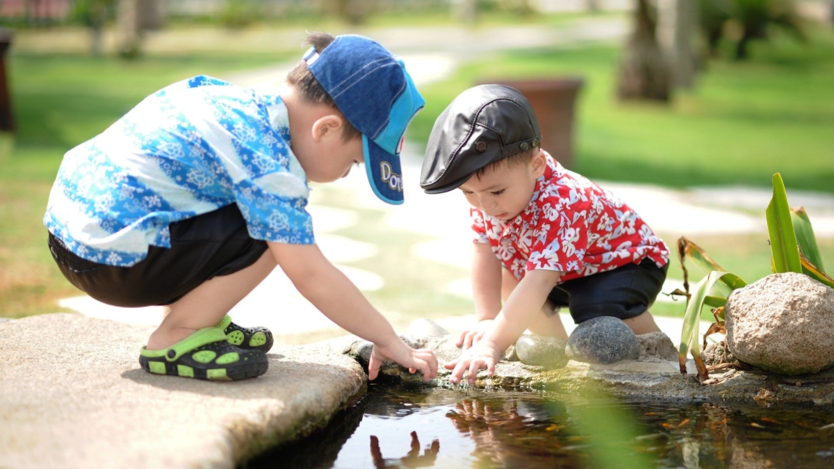 Two young children play together at the edge of a pond