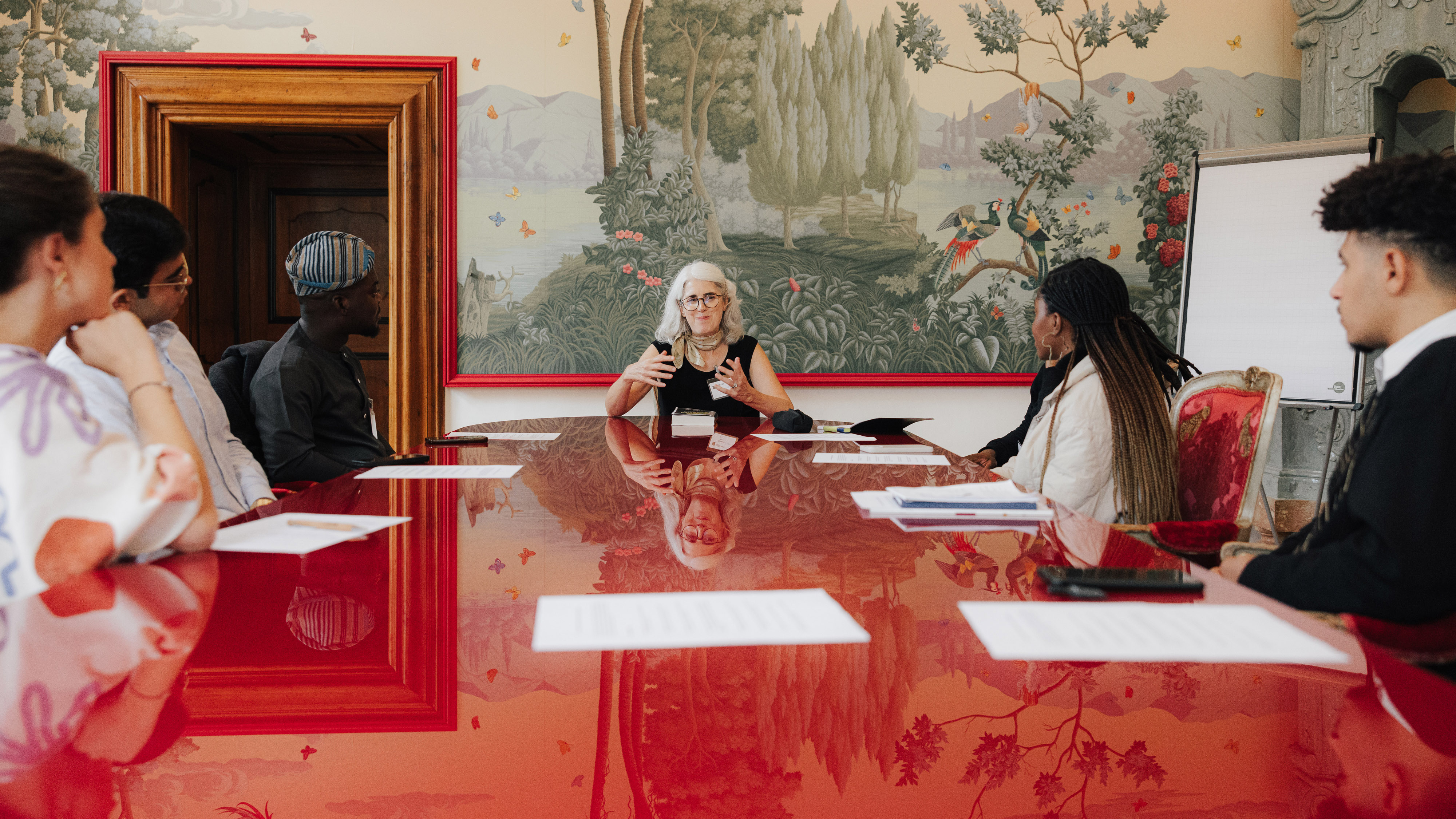 a diverse group of younger and older people sit around a table in the Red Salon of Schloss Leopoldskron during a Salzburg Global session