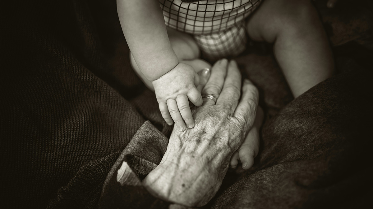 an image of an elderly hand holding the hand of an infant