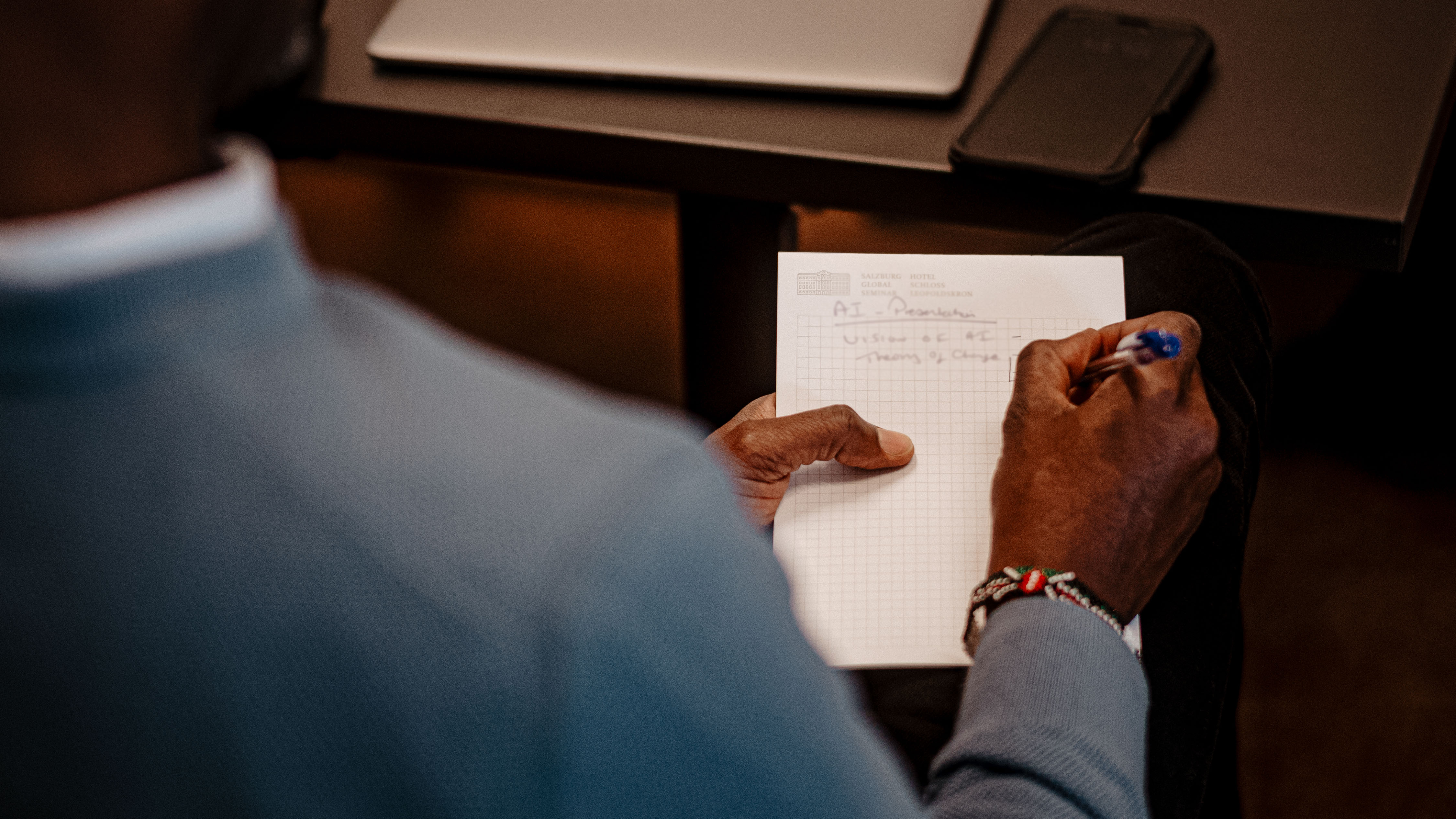 A view over a man's shoulder of him writing notes on a notepad.
