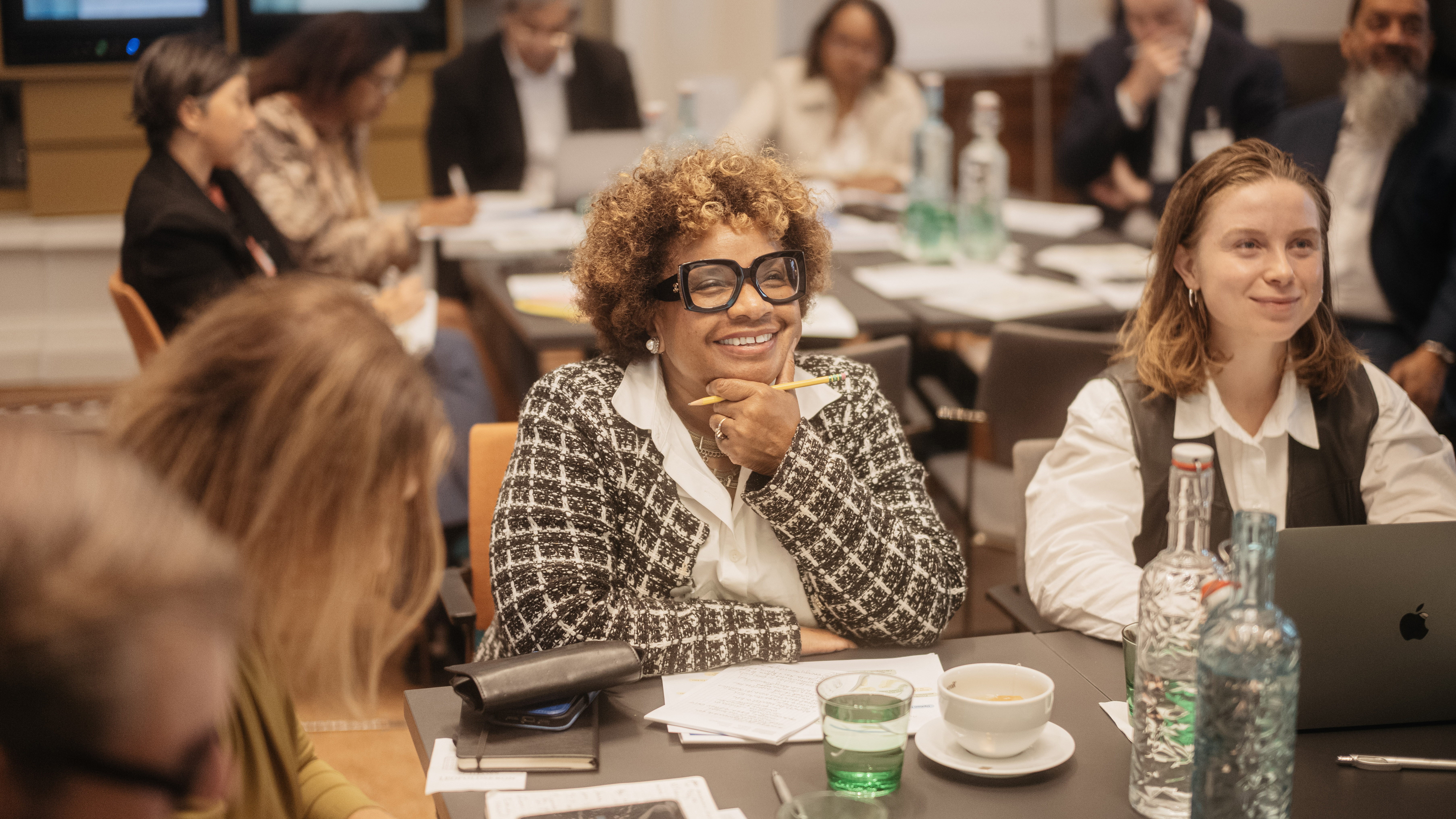 Lynn McNair, a woman with curly hair and glasses, smiles and looks attentively at a speaker who is out of sight in the Gallery of Schloss Leopoldskron.