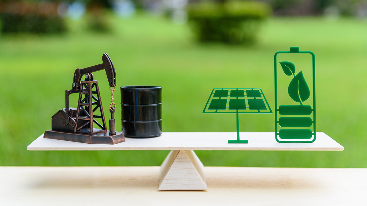The image shows a scale balancing between oil-related symbols (an oil pumpjack and barrel) on one side and clean energy symbols (a solar panel and battery with a leaf) on the other, representing the contrast between fossil fuels and renewable energy.
