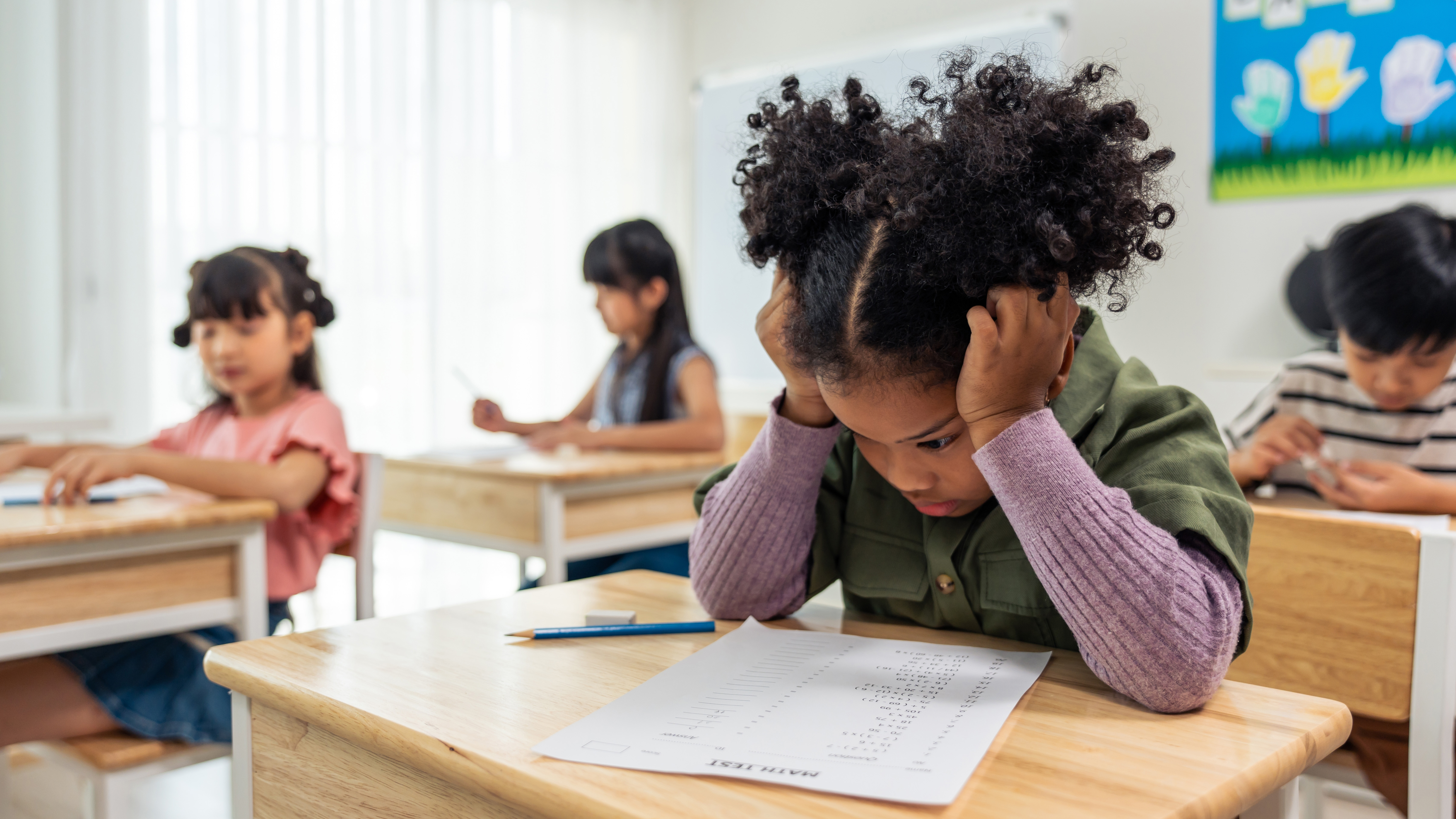 A young black girl doing an exam in a classroom, who appears upset and frustrated.