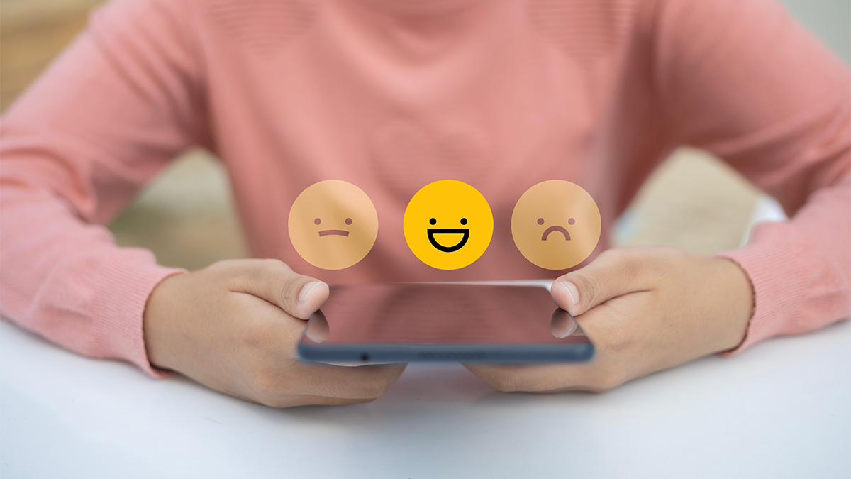 A girl wearing a pink shirt holds a tablet with three emoticon faces above it. 